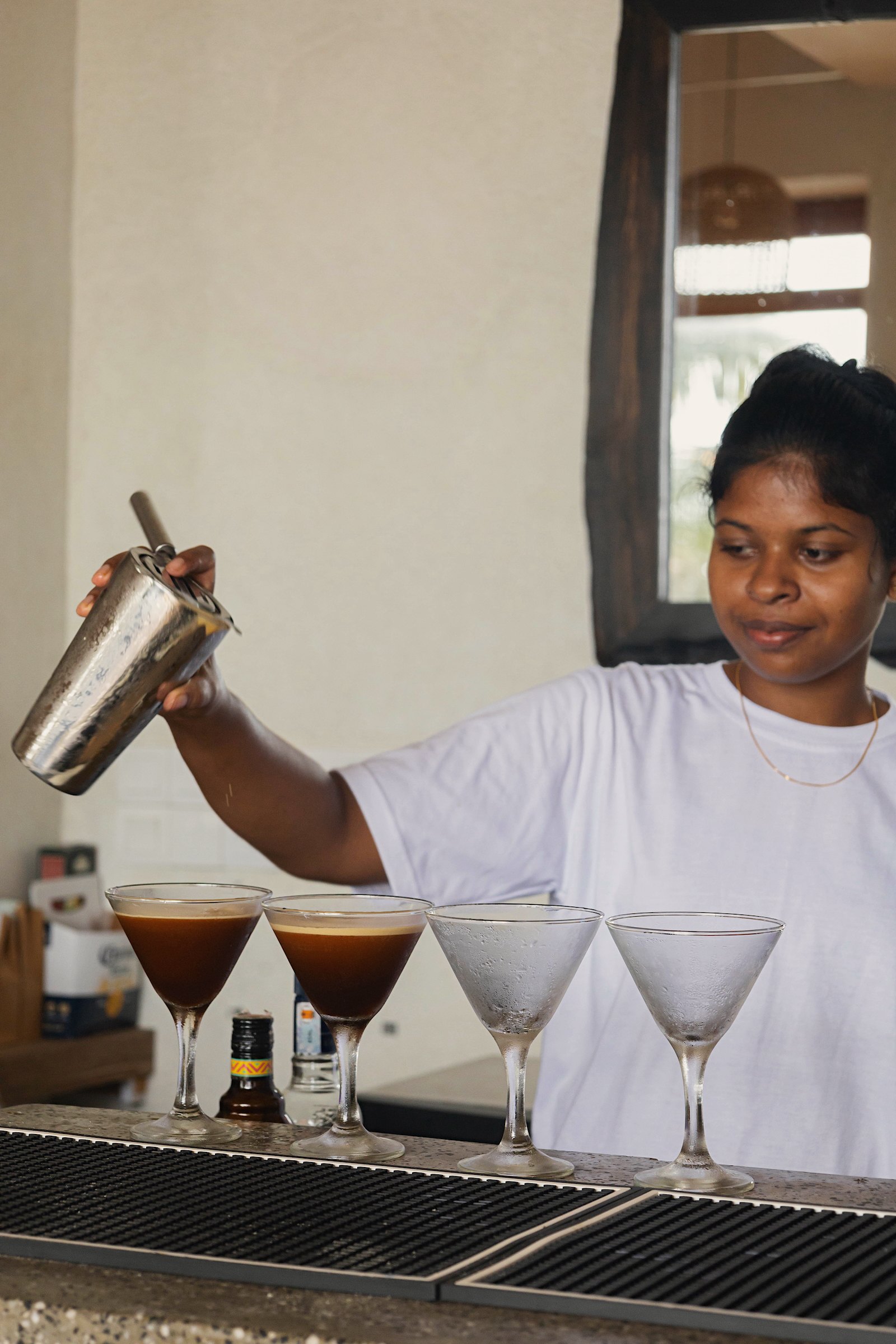 A bartender pouring cocktails into martini glasses