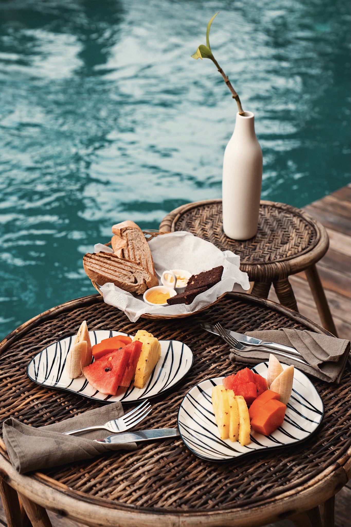 Breakfast of fresh fruit and toast on a rattan table beside the pool