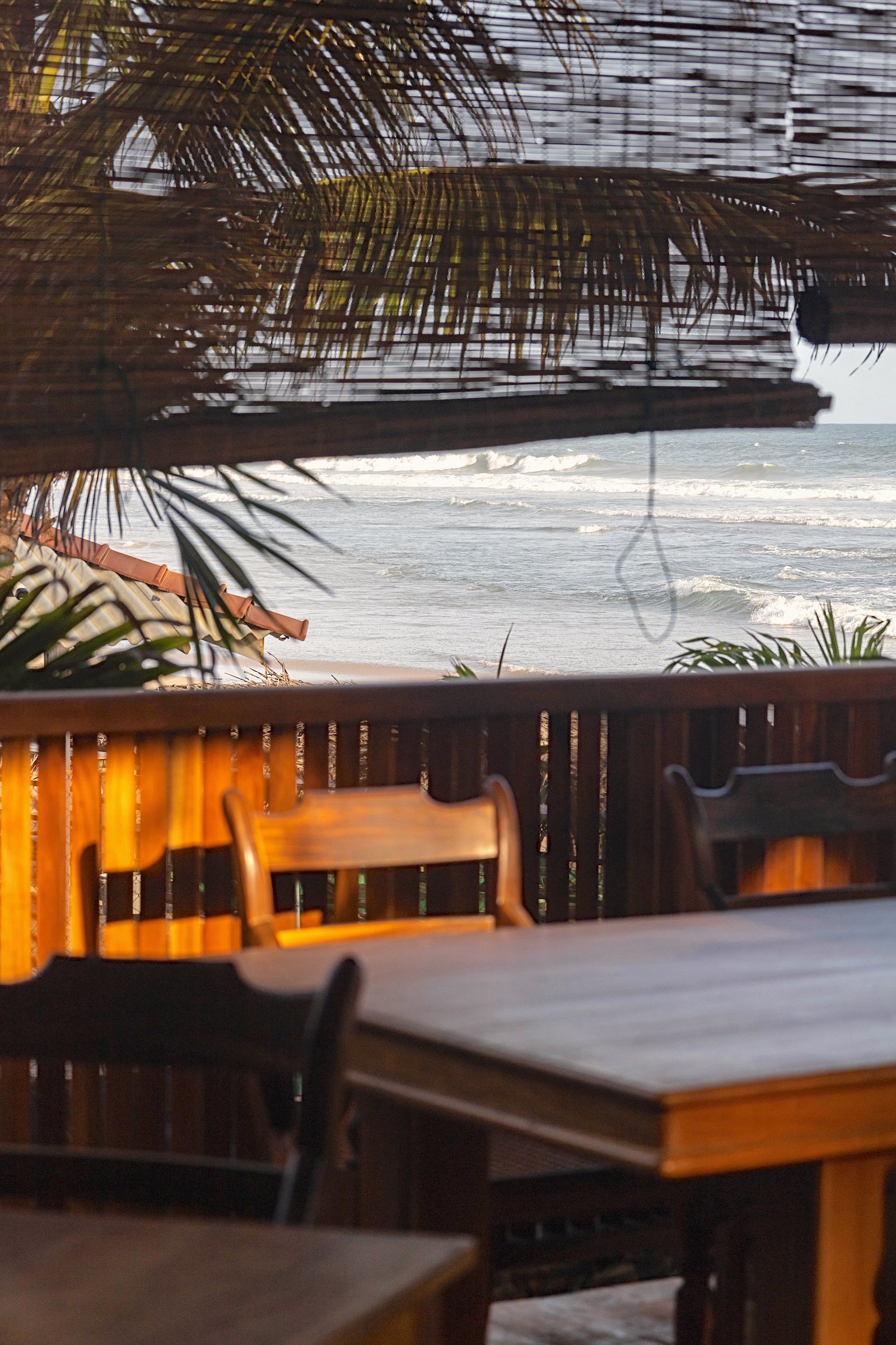 Dining tables under a rolled bamboo blind, looking out to the sea