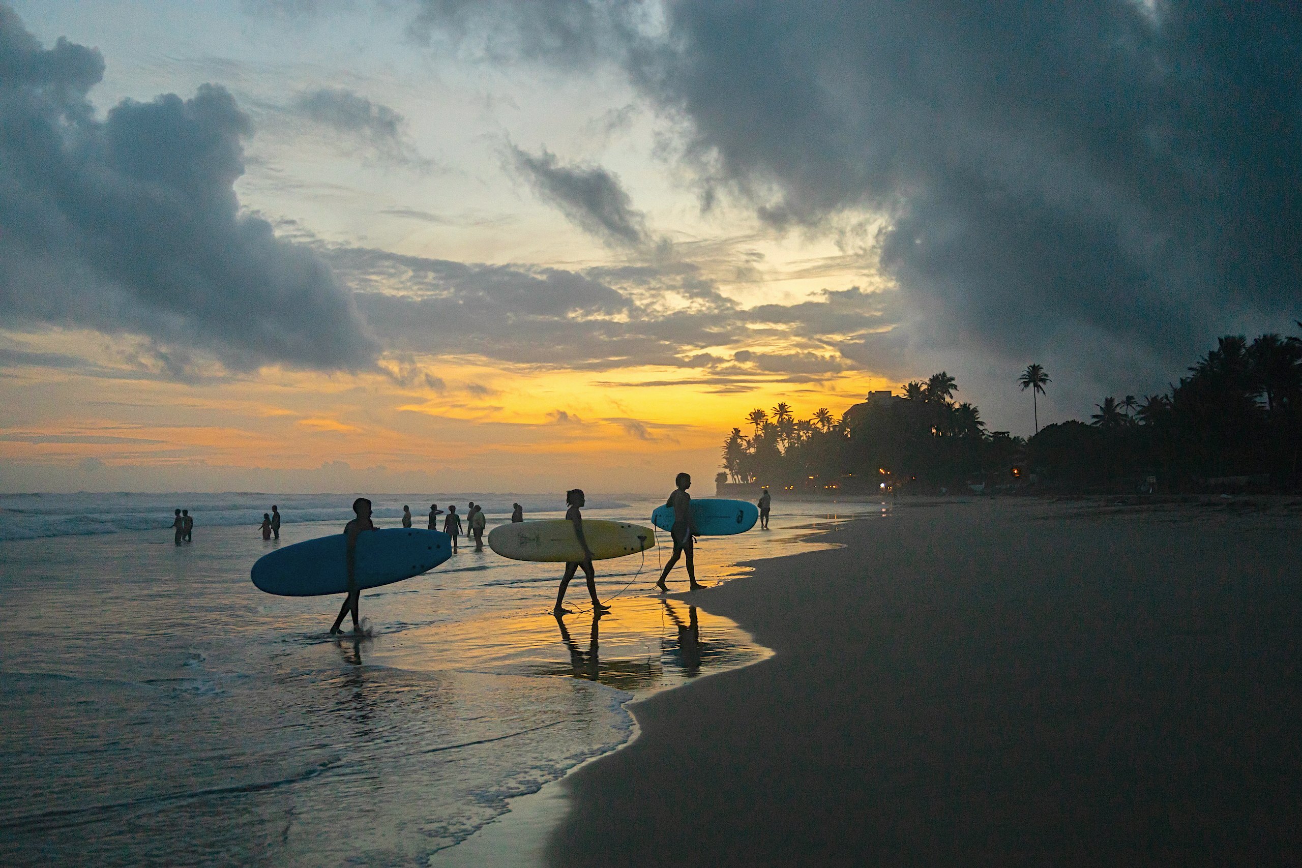 Surfers carrying their boards along the beach at dusk